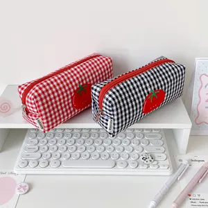 Detailed view of red and black checkered tomato pencil bags on a white desk setup