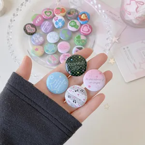 Close-up of four 25mm mini cartoon badges in hand with pastel decorative patterns