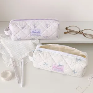 Vue détaillée des trousses en coton matelassé avec motifs nœuds et étiquette marque.