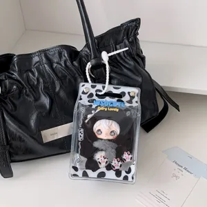 Close-up of a cow-print transparent plush doll display pouch hanging on a black bag.