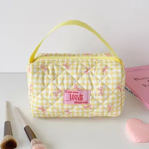Detailweergave van een geel geruite gewatteerde make-uptas met roze stoffen patch.