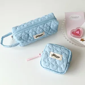 Gros plan d'une trousse bleu clair matelassée en forme de cœur et d'une pochette assortie.
