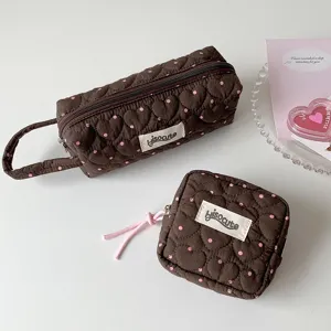 Gros plan sur une trousse matelassée marron avec des pois roses et des motifs de cœur.