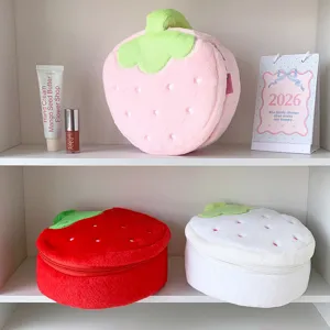 Soft plush strawberry makeup bags in three colors displayed with lifestyle props