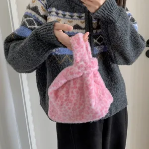 Close-up of a stylish pink leopard print plush knot handbag being held by a model