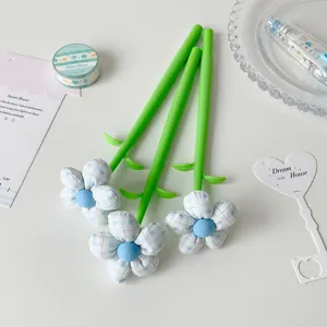 Macro detail of blue checkered fabric flower pens with green stems on a white desk.