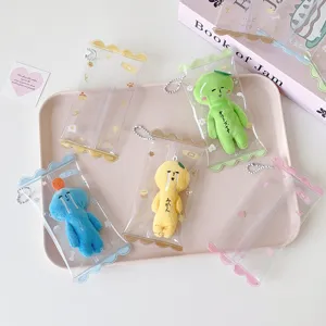 Transparent PVC mini doll display pouches with colorful plush figures on a pink tray.