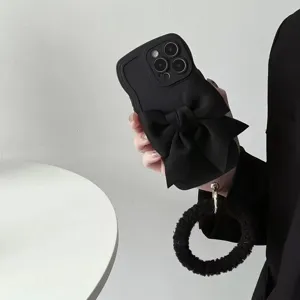 Dettaglio della custodia per telefono nera ondulata con grande fiocco e cinturino in peluche.