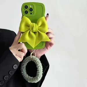 Custodia per telefono verde ondulata con grande fiocco in tessuto e cinturino in peluche.