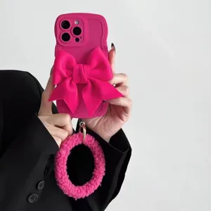 Primo piano di una custodia per telefono rosa ondulata con grande fiocco 3D e anello in peluche.