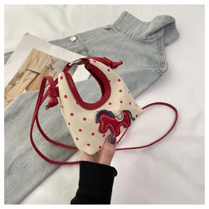 Primer plano de un mini bolso bandolera de lona con lunares rojos y un parche de caballo.