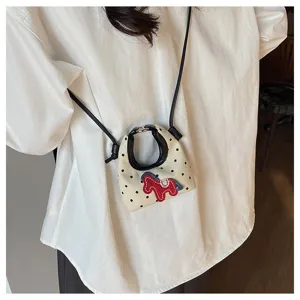 Primer plano de un mini bolso bandolera de lunares con un aplique de caballo rojo.