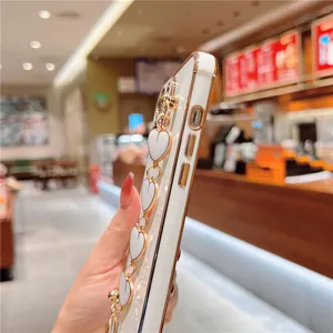 Detailed view of white electroplated phone case with elegant gold heart chain bracelet.