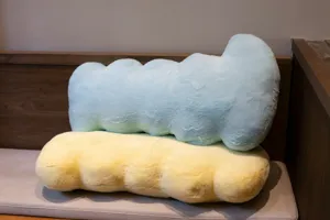 Detailed view of soft plush irregular long pillows in blue and yellow colors on sofa.