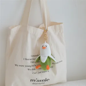 Cute banana duck plush keychain hanging on canvas tote bag, soft stuffed toy pendant for gifts.