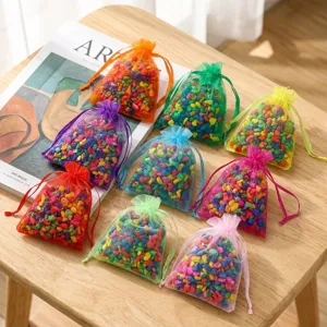 Colorful organza drawstring sachets filled with scented stones, displayed flat on a wooden table.