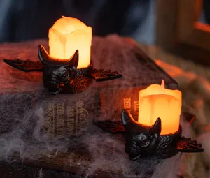 Close-up of Halloween LED candle with black bat-shaped base glowing in orange light.