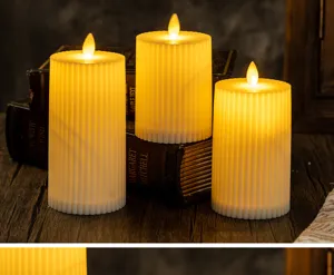 Set of three ribbed white LED pillar candles with warm glowing flame tips on vintage books