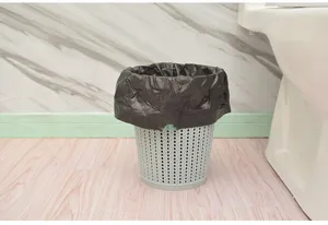Bolsa de basura negra con cordón ajustable en papelera gris, vista detallada en el baño.