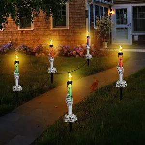 Decorative Halloween skeleton hand candle stakes glowing in a dark garden pathway