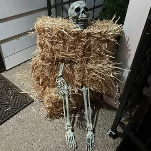 Realistic Halloween skeleton set decorative parts sticking out of a rustic hay bale on porch