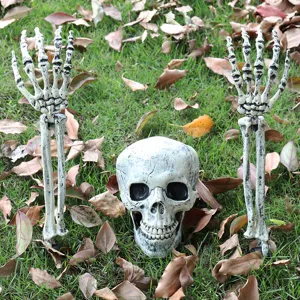 Realistic Halloween skeleton head and hand stakes installed on a lawn with autumn leaves.
