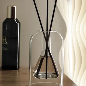 Detalle de difusor de vidrio minimalista con botella arqueada única y varillas negras.