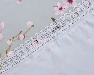 Close-up detail of grey cotton linen tablecloth featuring pink cherry blossoms and white lace trim.