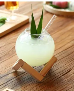 Close-up of clear round glass cup with wooden stand and straw on rustic wooden table.