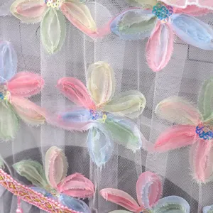 Primer plano de tela de malla blanca con bordado floral pastel colorido y lentejuelas brillantes.