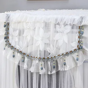 Elegante funda antipolvo de encaje blanco para lavadora con patrón floral y flecos de cuentas.