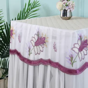 Detalle de la funda antipolvo para lavadora de encaje blanco con bordado floral morado.