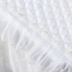 Primer plano detallado de la funda antipolvo acolchada blanca con delicados volantes encaje.