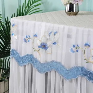 Detalle de funda para lavadora de encaje con bordado floral azul y dobladillo ondulado.