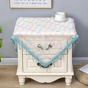 Hermosa funda antipolvo cuadrada con mariposas coloridas y flecos de cuentas azules en la mesa.