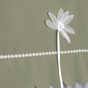 Nahaufnahme der grünen Stoffabdeckung mit weißer Chiffonblume und eleganter feiner Spitzenborte.