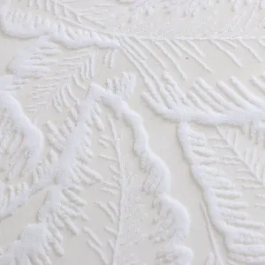 White lace fabric close up showing detailed embossed fern leaf texture pattern for home decor.