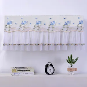 Gedetailleerd uitzicht van witte kanten wand-airconditioner stofhoes met blauw borduurwerk.