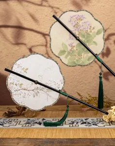 Gros plan détaillé d'un éventail traditionnel chinois avec imprimé floral et gland vert.