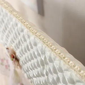 Primo piano della copertura antipolvere trapuntata per TV con delicato bordo in pizzo e decorazione.