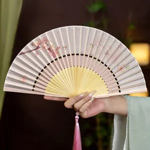 Éventail pliant de style traditionnel chinois avec motifs floraux et pompon rose.