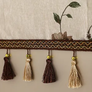 Detalle en primer plano de funda textil con bordado floral y flecos decorativos elegantes.