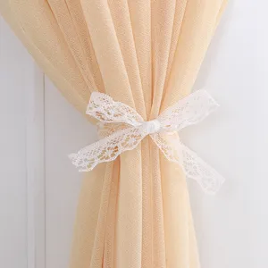 Primo piano dettagliato di una tenda color champagne semitransparente con fiocco di pizzo bianco.