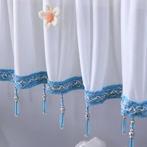 Détail de rideau transparent blanc avec belle bordure en dentelle bleue et glands perlés.