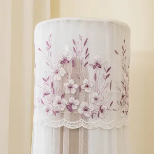 Dettaglio della copertura per condizionatore in rete bianca con ricamo floreale viola.