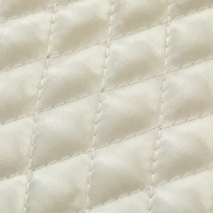 Vista detallada de tela crema con patrón de rombos acolchado, textura lisa, costuras.