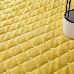 Primer plano detalle de tela acolchada amarilla con diseño de costuras de rombos, suave.
