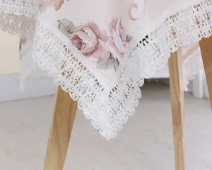 Close-up detail of vintage floral tablecloth with pink roses and elegant white lace edge.