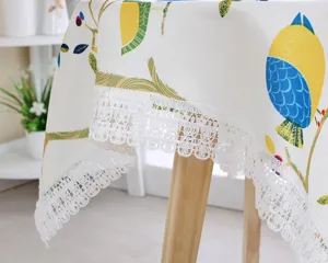 Close-up of cotton linen tablecloth with blue bird print and white lace trim for dining table.