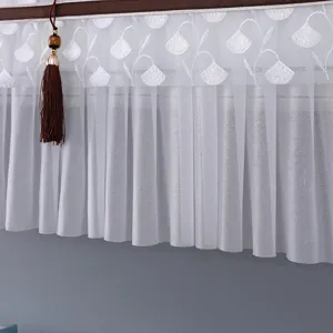 Dettaglio copridispositivo climatizzatore, tenda in pizzo bianco con nappa marrone elegante.